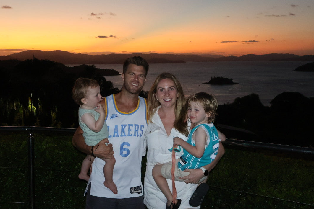 Family of four posing for a photo against a sunset backdrop with mountains and water.