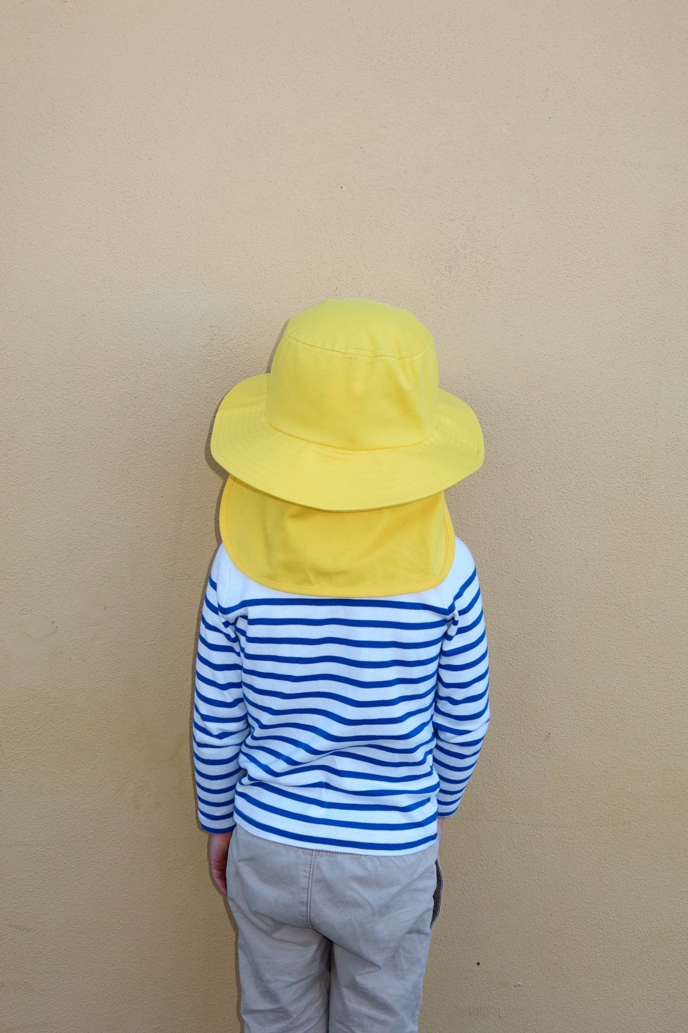 Back view of a child wearing a bright yellow Luma sun hat with a protective neck flap