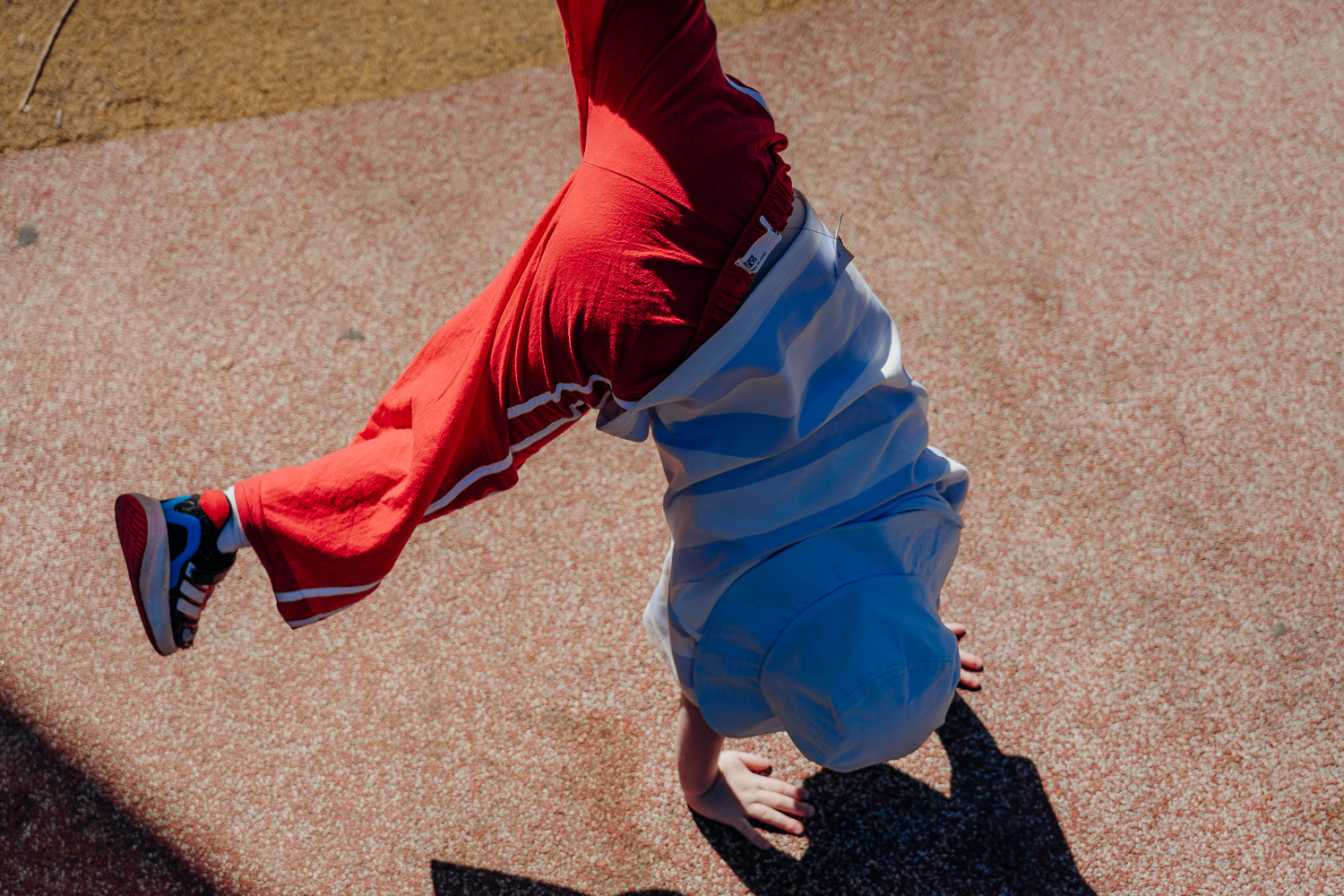 Kid in red pants and a blue luma hat thats buckled on to stop it falling off doing a handstand.