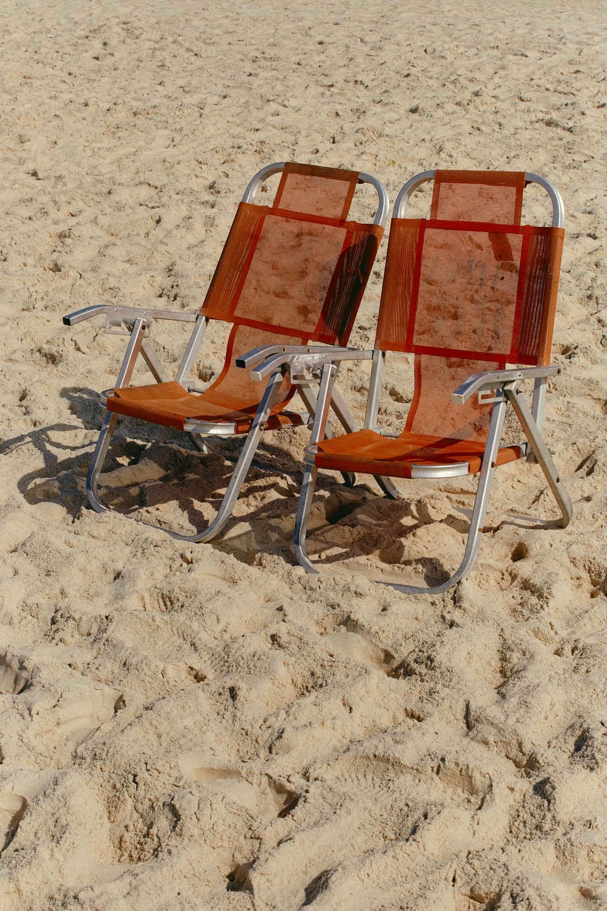Two orange lounge chairs on a sandy beach