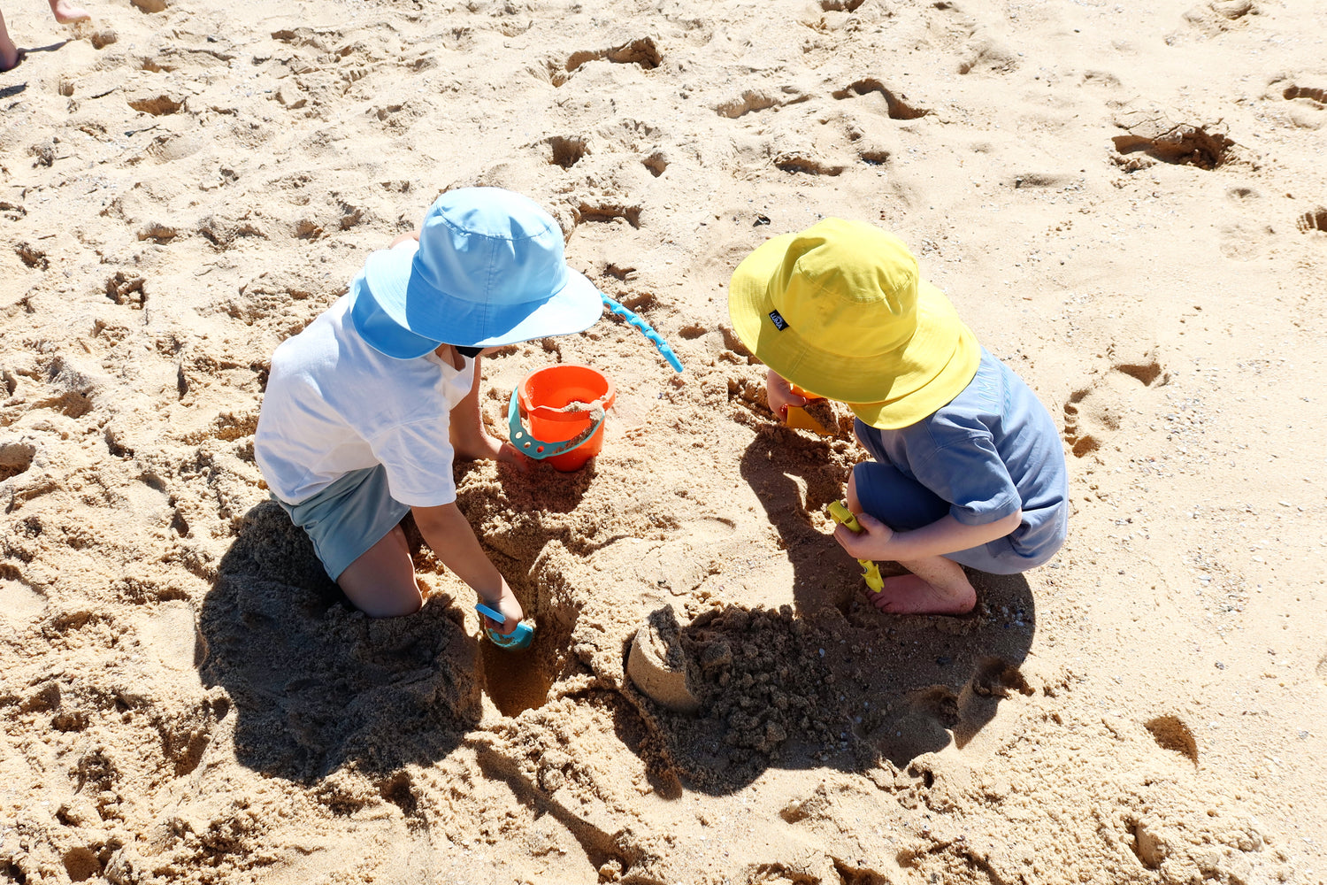 Kids in blue and yellow sun hats playing in the sand